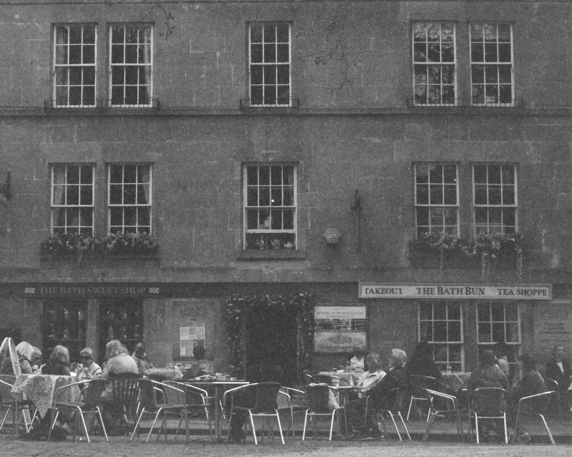 The Bath Bun Teashoppe at Bath, England with its Georgian terrace with three storeys of sash windows, and people seated at outdoor café tables