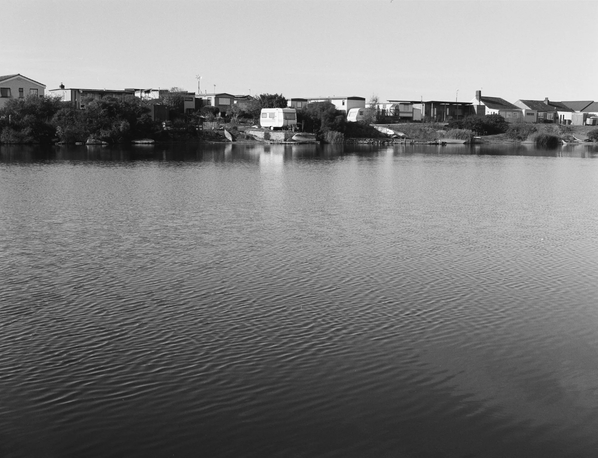 A water channel with patterned ripples and reflecting caravans and houses along the far shore at Snettisham, Norfolk Coast, England