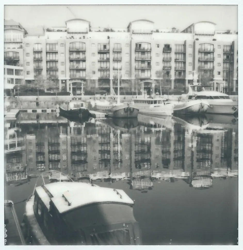 Riverside apartment block and moored boats reflected in the still water of St Katherine's Dock