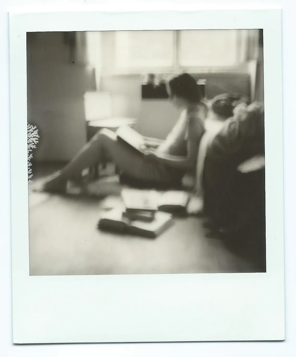 A woman reading on the floor, books scattered around her, window light behind